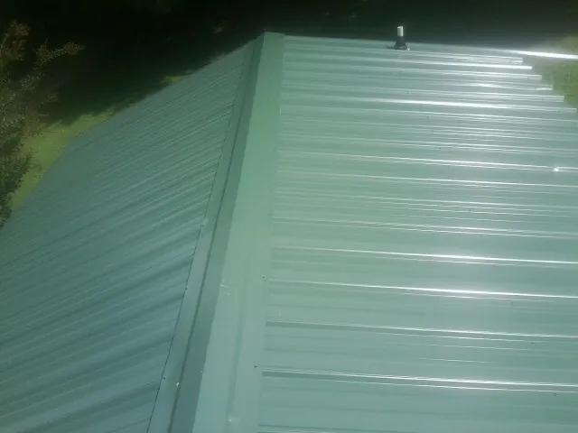 New green metal panels meeting at the ridge of a roof — Flat Roof Repair work by our crew in Duquesne