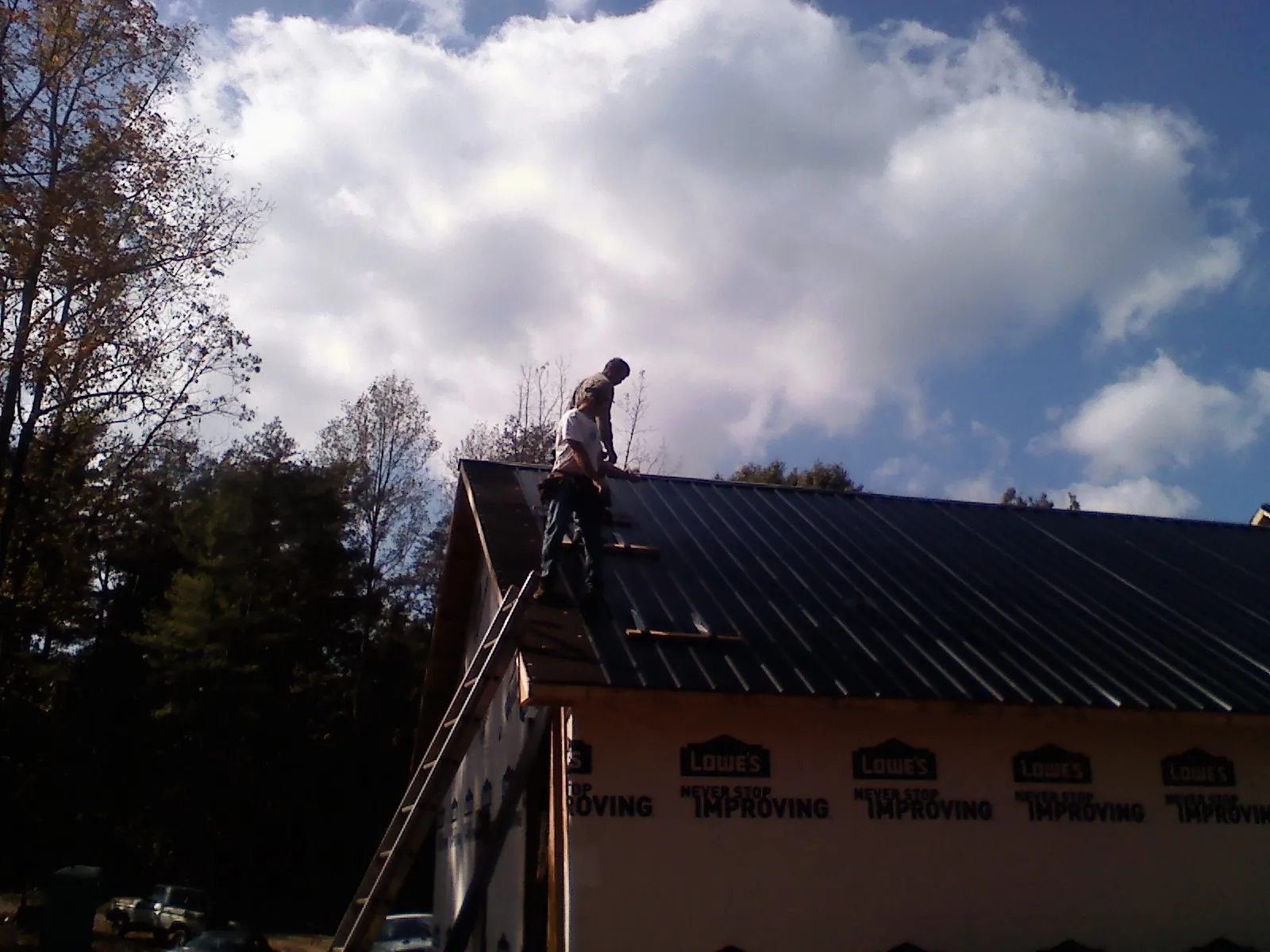 Roofer fastening dark metal panels high against a cloudy sky, from a Roof Inspection job in Duquesne