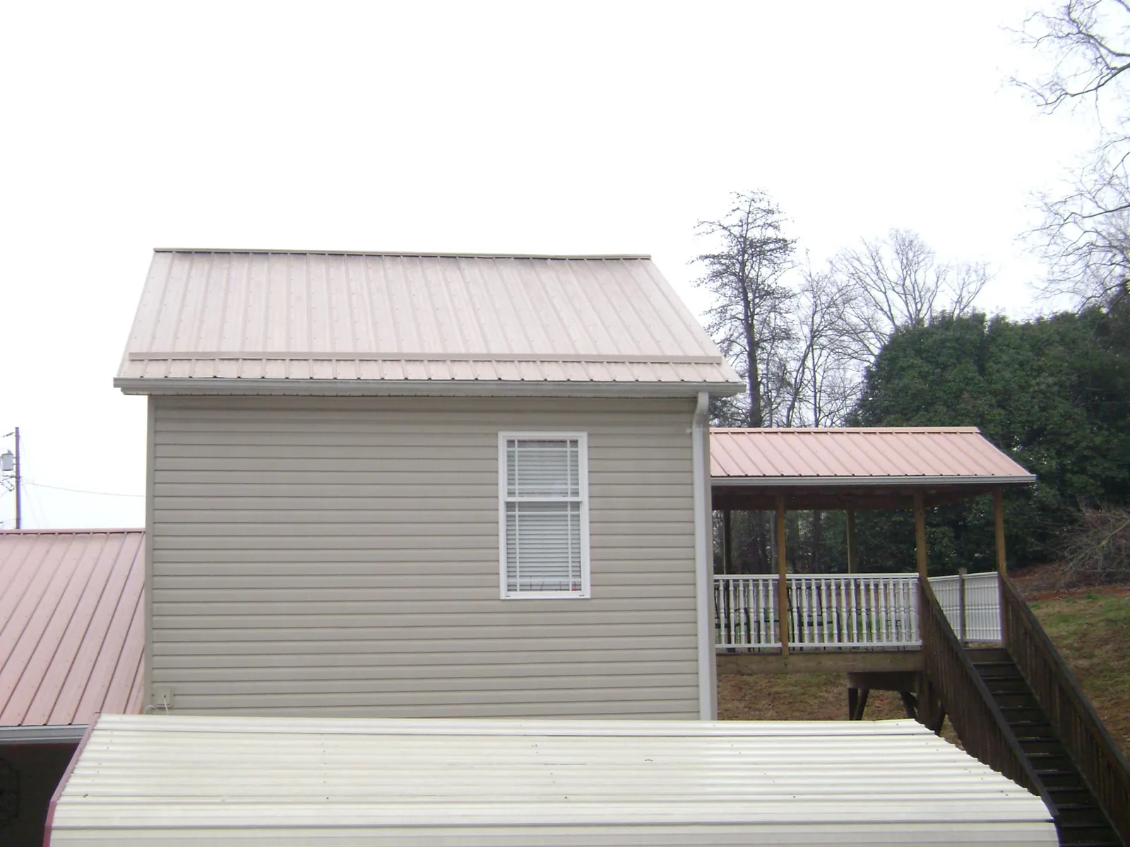Tan metal roofs on a two story addition and attached porch, from a Roof Replacement job in Duquesne